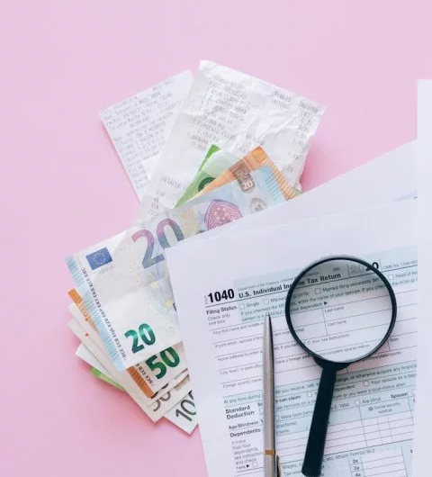 Stos banknotów i lupa na stole, symbolizujące analizę finansową.