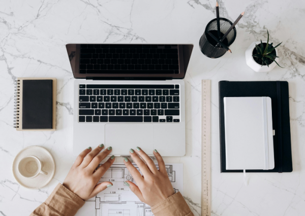 Skoncentrowana Praca nad Rozwiązaniami Finansowymi Osoba w brązowej koszuli długim rękawem pracująca na MacBooku Pro obok białego kubka ceramicznego.